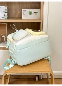 Close-up detail shot of a pastel color-blocked school backpack with mesh pocket on wooden stool.