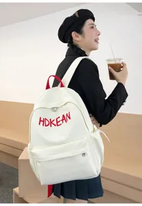 Une jeune femme portant un sac à dos blanc minimaliste avec broderie de lettres rouges