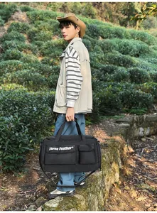 Asiatisches männliches Model mit großer schwarzer Outdoor-Reisetasche im grünen Teegarten