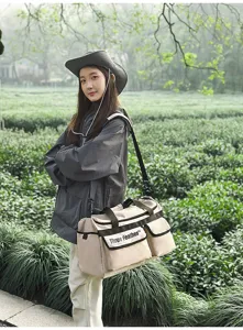 Modell trägt eine große beige Reisetasche in einer üppigen und grünen Teeplantage.