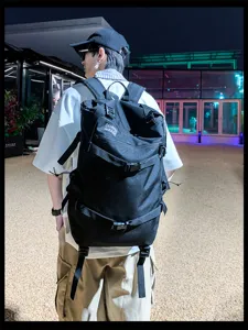 Achteraanzicht van een man met een grote zwarte tactische wandelrugzak buiten in de nacht.