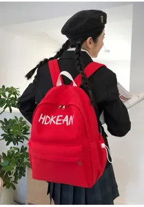 Sac à dos d'école en toile rouge avec logo blanc porté par une étudiante en blazer