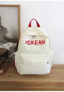 Sac à dos minimaliste en toile blanche avec broderie HDKEAN rouge sur table en bois
