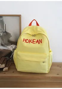 Vue détaillée d'un sac à dos scolaire jaune avec des lettres brodées rouges sur bois