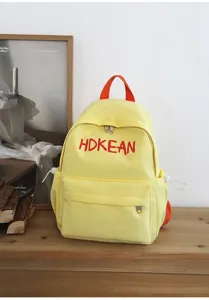 Détail d'un sac à dos scolaire jaune avec broderie HDKEAN rouge sur étagère bois