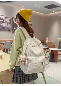 Vue de dos d'une fille portant un sac à dos d'école à carreaux crème avec un ours.