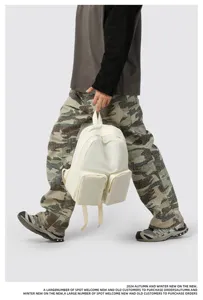 White canvas backpack with two front pockets held by a person in camouflage pants