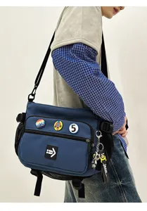 Detailed view of a blue utility messenger bag with pins and keychain accessories.