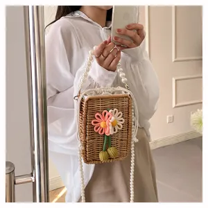 Gros plan d'un sac en paille avec broderie florale et chaîne en perles élégante.
