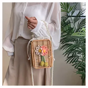 Gros plan d'un sac en paille tissé avec des fleurs colorées et une chaîne en perles
