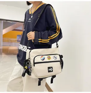 Detail view of large white canvas messenger bag with decorative badges and pins.