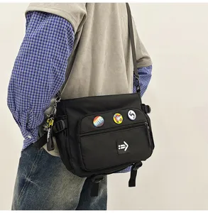 Close-up of a black messenger bag with workwear styling and colorful pin badges