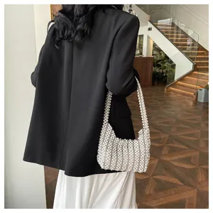 Detailansicht einer handgefertigten weißen Perlen-Unterarmtasche mit schwarzem Blazer.