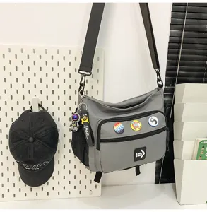 Side view of a grey unisex messenger bag featuring multiple badges and an astronaut charm