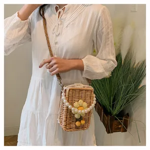 Détail d'un sac bandoulière en paille tressée avec fleur en tricot et chaîne de perles.