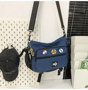 Durable navy blue utility messenger bag featuring decorative badges and a wide strap