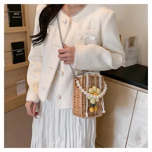 Détail d'un sac à bandoulière en paille tressée avec chaîne en perles et fleur.