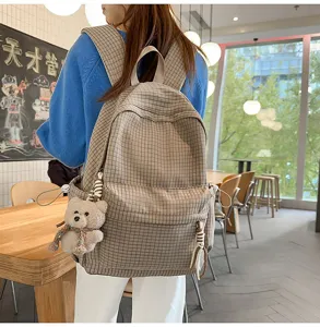 Modèle avec sac à dos à carreaux beige et pendentif ours dans un cadre chaleureux.
