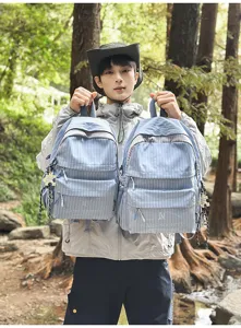 Mannequin tenant deux sacs à dos à carreaux bleu clair dans un décor de forêt luxuriante