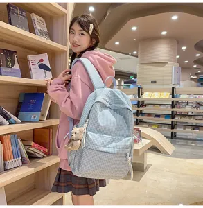 Gros plan d'un sac à dos scolaire à carreaux bleu clair avec breloque ours en bibliothèque
