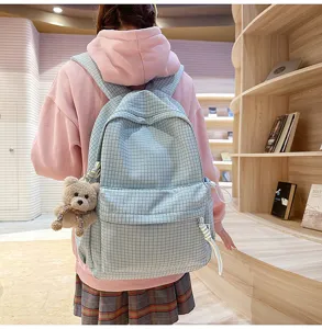 Étudiante portant un sac à dos à carreaux bleu clair avec un charm d'ours en peluche