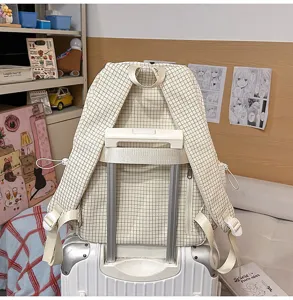Vue arrière du sac à dos d'école à carreaux fixé à la poignée de traction d'une valise