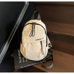Detailansicht einer minimalistischen beigen Streetstyle-Brusttasche auf einem schwarzen Buch.