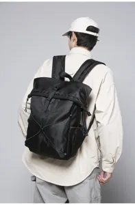 Close-up detail of a men's black roll-top commuter backpack with bungee cord design