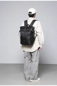 Back view of model wearing a black roll-top commuter backpack with buckle detail