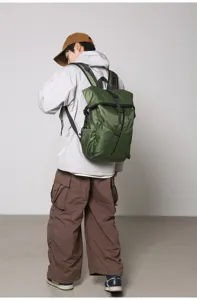Detailed rear view of a durable green roll-top backpack worn by a model in casual style