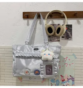 Detailansicht einer silbernen Ita-Tasche mit klarem Fenster, Plüschtier und Abzeichen