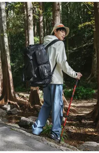 Back view of a hiker carrying a black multi-pocket sports bag in a scenic forest trail.