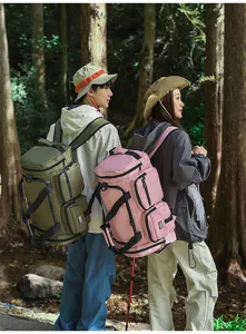 Two hikers wearing olive and pink large capacity travel duffel bags in the forest