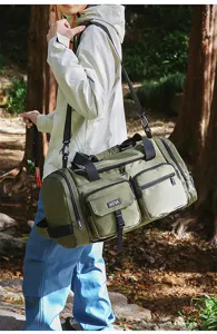 Man carrying a large olive green multi-pocket sports duffel bag in a sunny forest