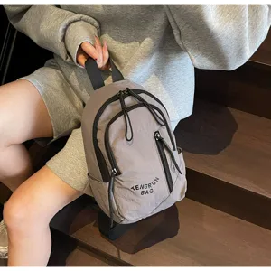 Graue Nylon-Techwear-Umhängetasche mit mehreren Reißverschlüssen auf hölzernen Treppe