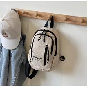 Kleine beige Umhängetasche für den Alltag, hängend an einer Wandgarderobe