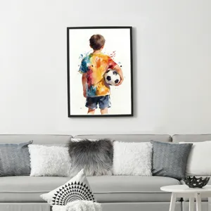Watercolor sports canvas art of a boy with a soccer ball displayed above a grey sofa.