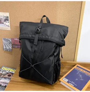 A high-quality detail view of a black roll-top commuter backpack placed on a wooden desk