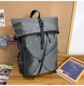 Detail of grey roll-top backpack on wooden desk with books and cork board background