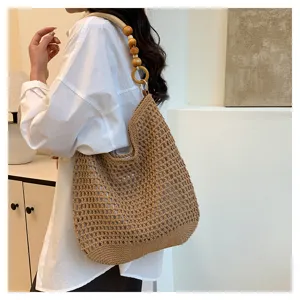 Détail d'un sac cabas en tricot ajouré avec bandoulière en perles de bois porté par un modèle