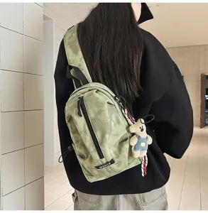 Detail of a sage green canvas chest bag with cute bear keychain for outdoor casual use.