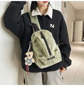 Detailed view of a green casual canvas sling bag featuring a cute teddy bear keychain