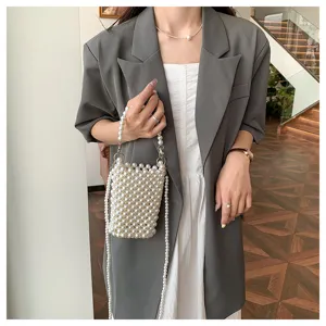 Detailed view of an elegant hand-woven pearl phone bag styled with a grey blazer