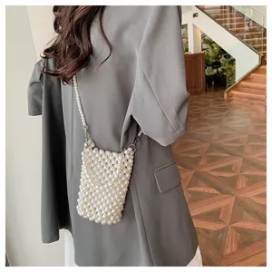 Close-up of elegant white woven pearl crossbody phone bag worn with grey blazer