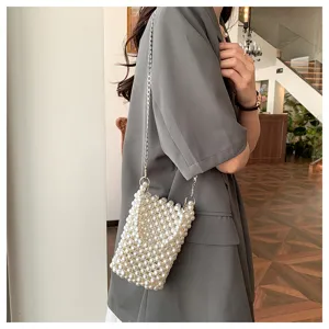 Close-up detail of a stylish white pearl woven crossbody cell phone bag worn by a model