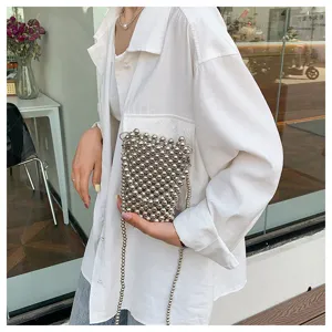 Detail shot of a stylish silver beaded mini crossbody phone bag held against a white shirt