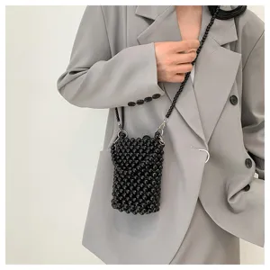 Close-up detail of a handmade black beaded crossbody phone bag worn over a minimalist grey blazer