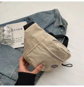 Nahaufnahme einer beigen Nylon-Brusttasche, die über einer Denim-Jacke gehalten wird