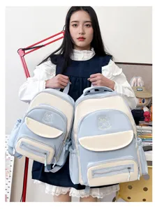 Asian female model holding large and small blue preppy student backpacks side by side