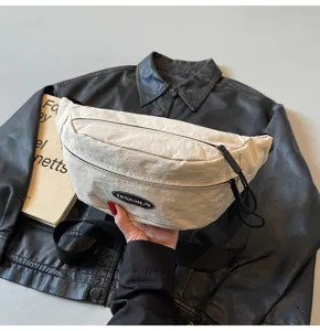 Detailansicht der cremefarbenen Nylon-Brusttasche mit schwarzem Logo-Patch auf Lederjacke.